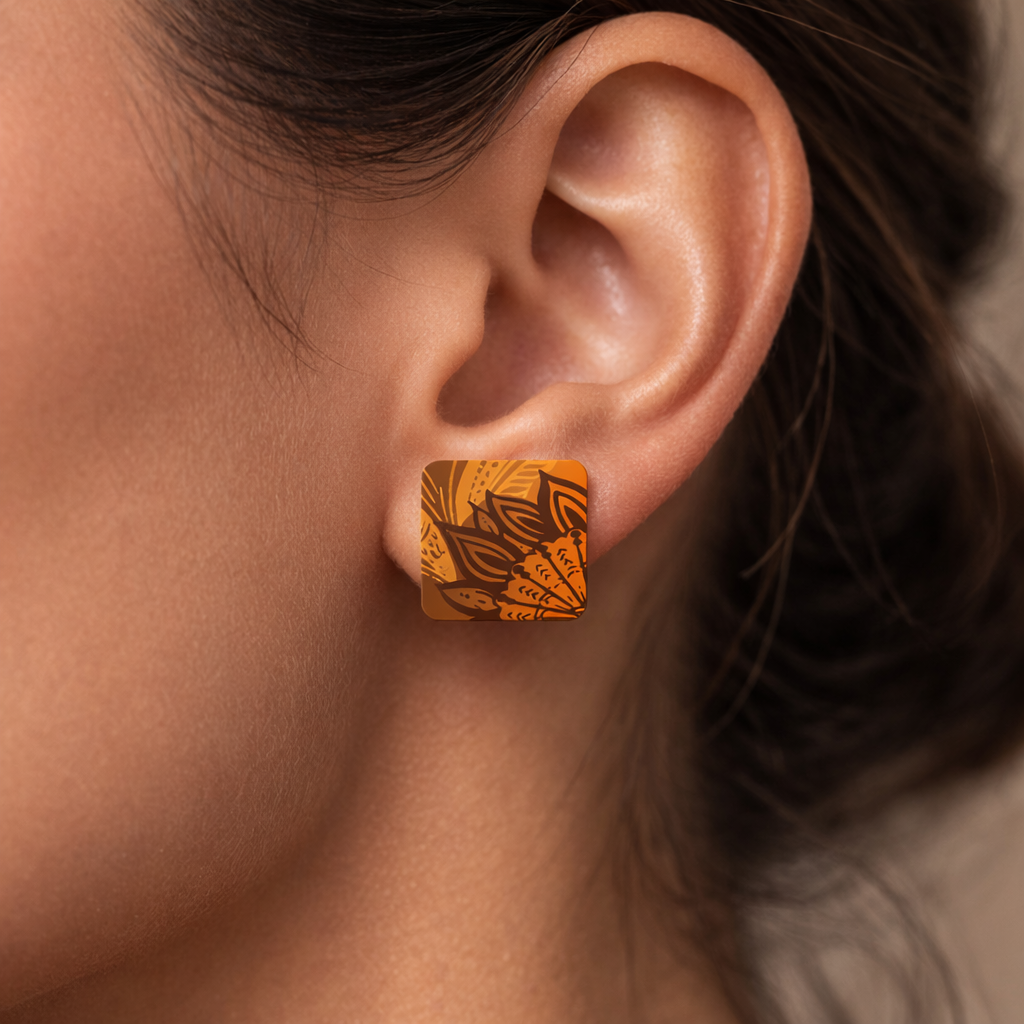 Close-up of an ear wearing a decorative orange earring with intricate patterns.