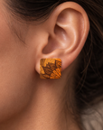 Close-up of an ear wearing a decorative orange earring with intricate patterns.
