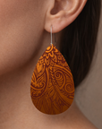 Teardrop-shaped earrings with intricate patterns worn by a person.
